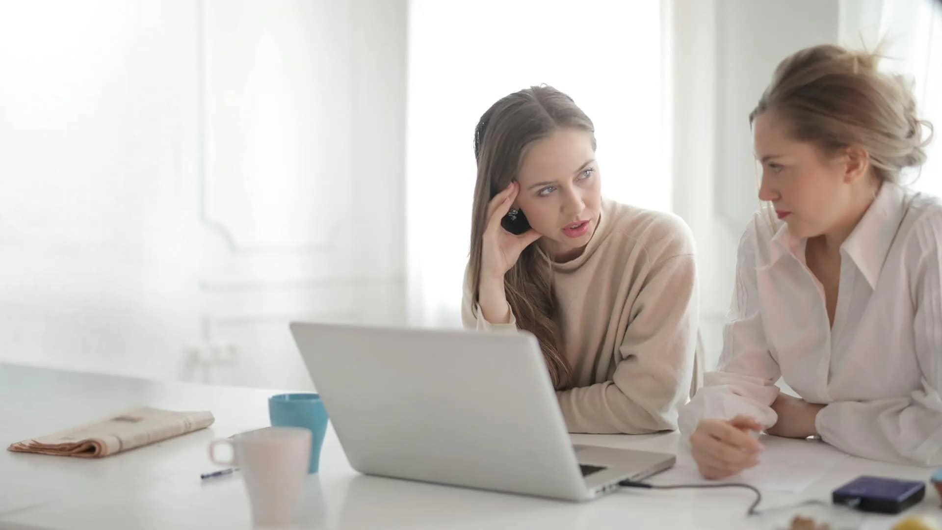 Two colleagues at a laptop, one listening on the phone